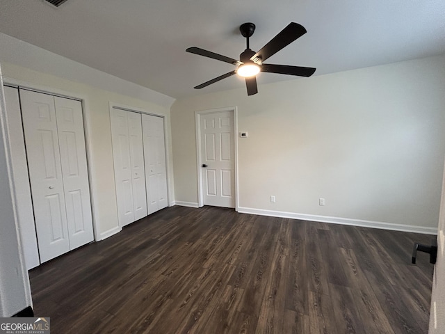 unfurnished bedroom featuring multiple closets, dark wood finished floors, baseboards, and a ceiling fan