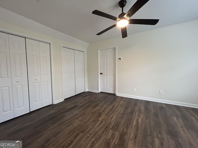 unfurnished bedroom featuring baseboards, dark wood finished floors, a ceiling fan, and multiple closets