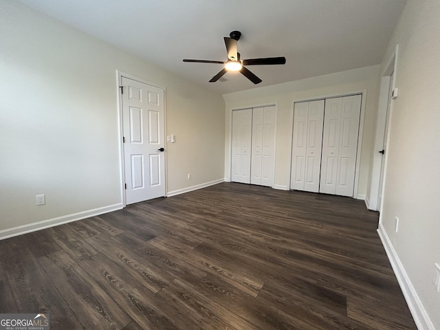 unfurnished bedroom with dark wood-style floors, ceiling fan, two closets, and baseboards