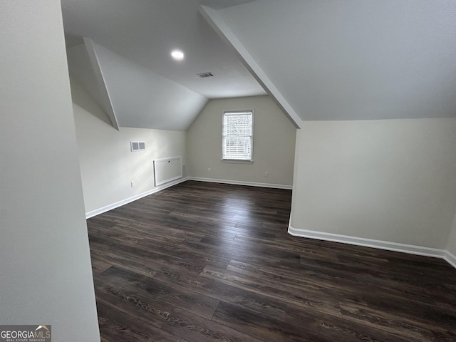 additional living space with baseboards, visible vents, vaulted ceiling, and dark wood-style flooring