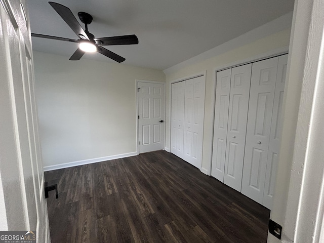 unfurnished bedroom with ceiling fan, baseboards, dark wood-type flooring, and multiple closets