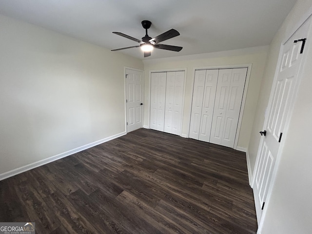 unfurnished bedroom featuring ceiling fan, dark wood finished floors, baseboards, and two closets