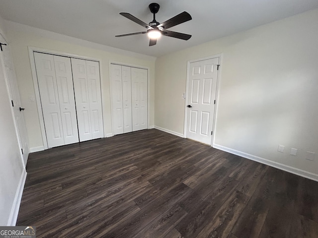 unfurnished bedroom with ceiling fan, dark wood-style flooring, two closets, and baseboards