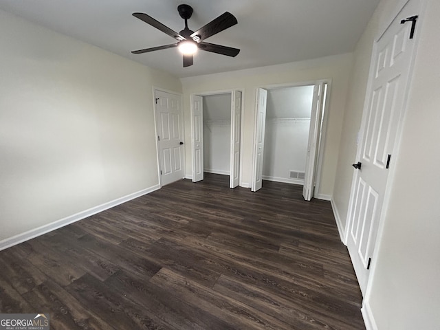 unfurnished bedroom with baseboards, dark wood-type flooring, visible vents, and multiple closets