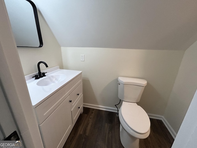 half bathroom with lofted ceiling, toilet, vanity, wood finished floors, and baseboards