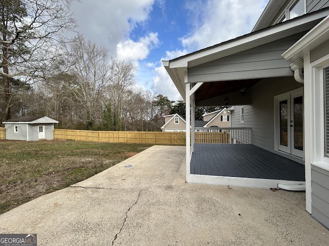 view of patio / terrace featuring an outbuilding, french doors, fence, a deck, and driveway