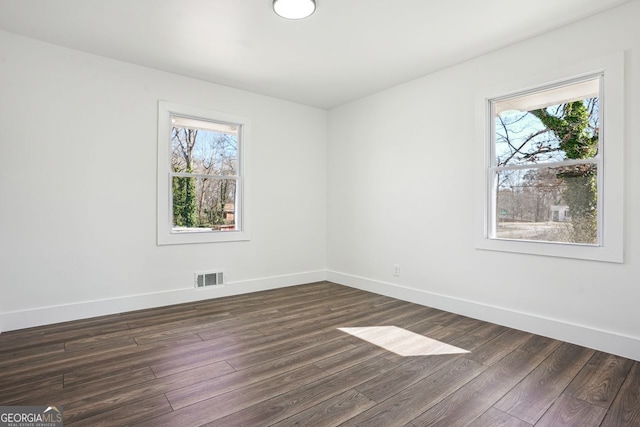 unfurnished room featuring a wealth of natural light, dark wood finished floors, visible vents, and baseboards