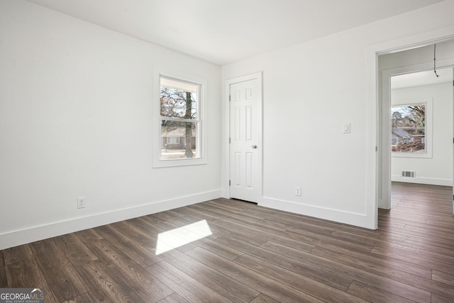 unfurnished bedroom featuring dark wood-style floors, multiple windows, and visible vents