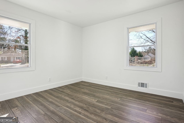 empty room featuring a wealth of natural light, dark wood finished floors, visible vents, and baseboards