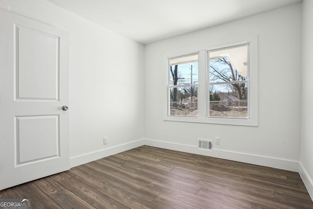 empty room featuring dark wood-style floors, visible vents, and baseboards