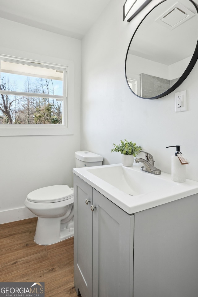 half bathroom with toilet, wood finished floors, visible vents, vanity, and baseboards