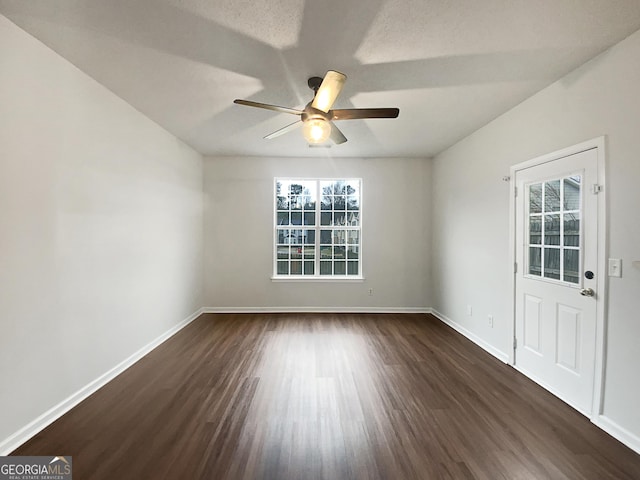 empty room featuring ceiling fan, dark wood finished floors, and baseboards