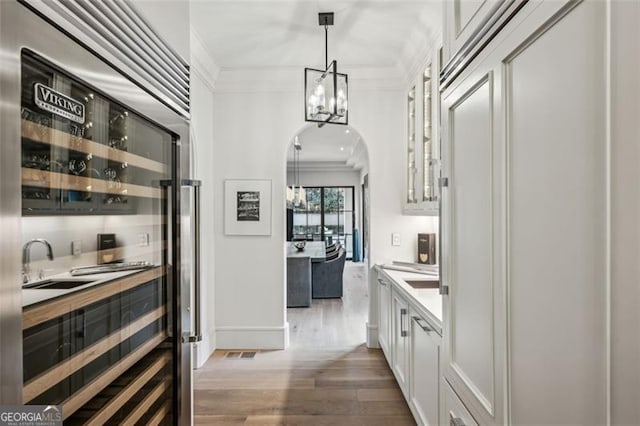 interior space featuring wood finished floors, arched walkways, ornamental molding, white cabinetry, and a notable chandelier