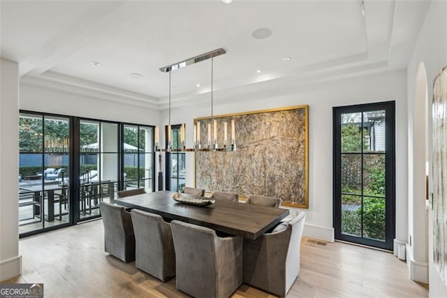 dining area with baseboards, a raised ceiling, arched walkways, and light wood finished floors