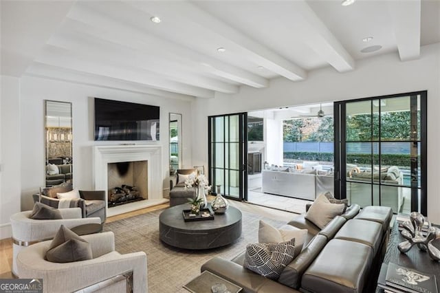 living area with a wealth of natural light, beam ceiling, a fireplace with raised hearth, and wood finished floors