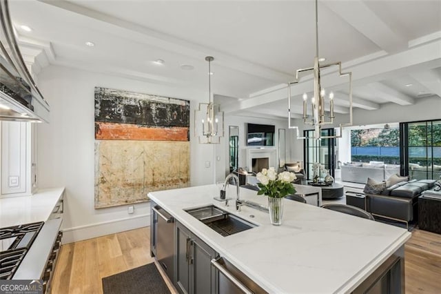 kitchen featuring beam ceiling, a notable chandelier, a sink, open floor plan, and light wood-style floors