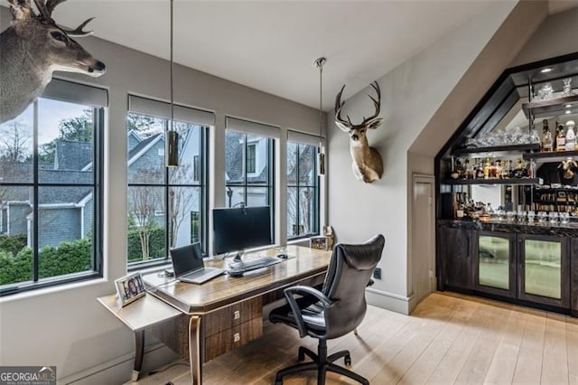 office space with a bar, baseboards, and wood finished floors