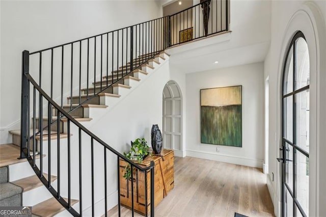 stairway with wood finished floors, baseboards, and a towering ceiling