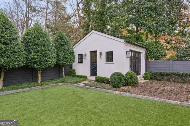 view of front of house featuring stucco siding, an outbuilding, a fenced backyard, and a front lawn