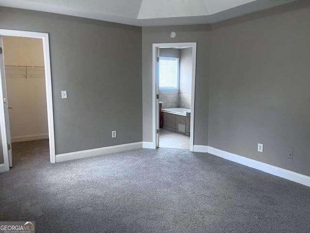 unfurnished bedroom featuring a walk in closet, a closet, light colored carpet, and baseboards