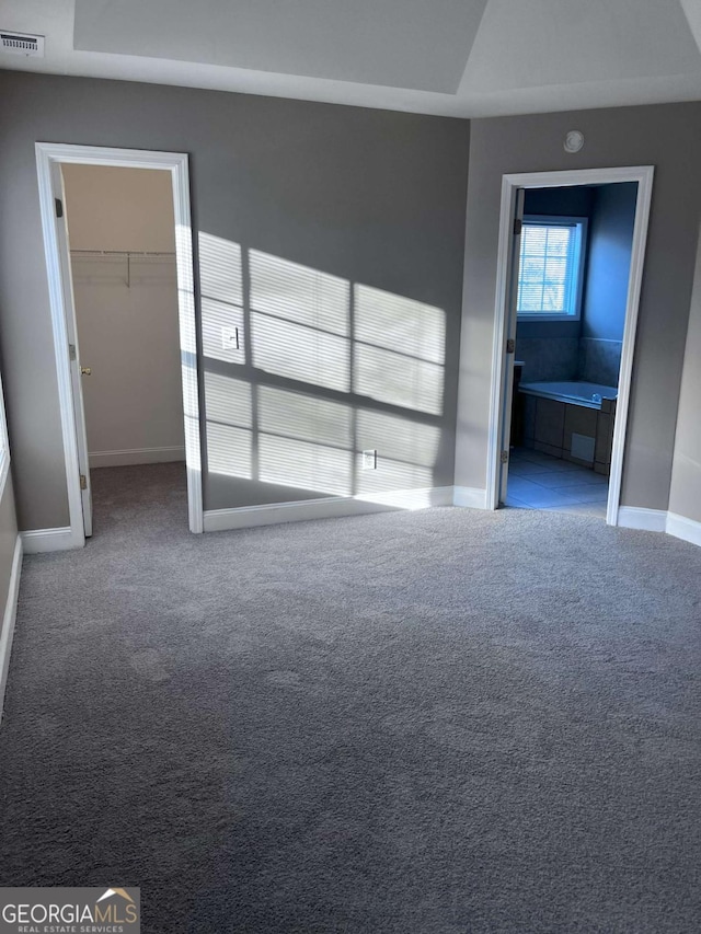 unfurnished bedroom featuring visible vents, baseboards, ensuite bath, carpet, and a spacious closet