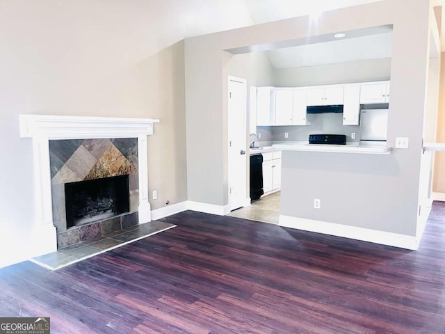 kitchen with white cabinets, a tile fireplace, wood finished floors, under cabinet range hood, and black appliances