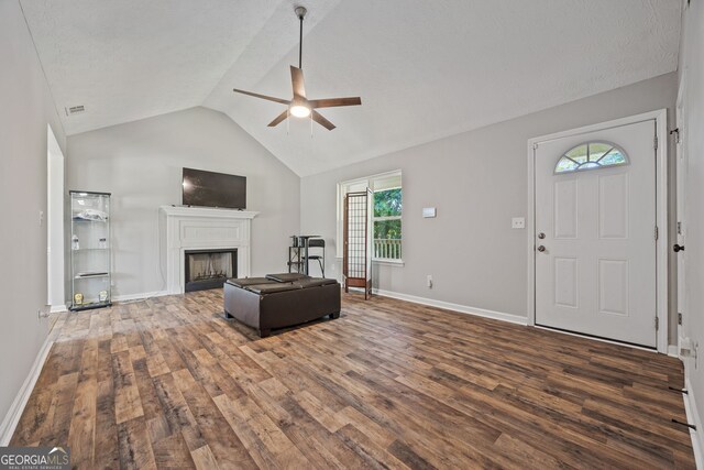 living area with dark wood-style floors, a ceiling fan, a lit fireplace, vaulted ceiling, and baseboards