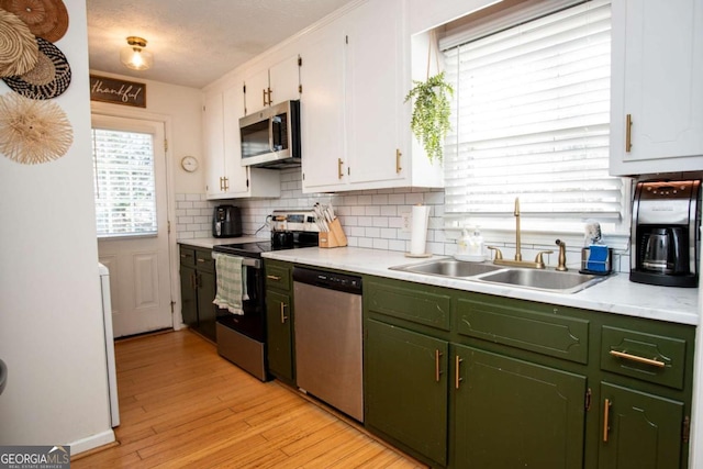 kitchen with decorative backsplash, stainless steel appliances, light countertops, green cabinets, and a sink