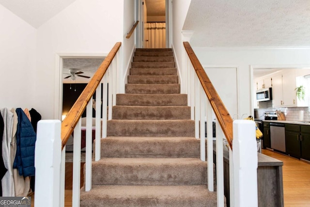 staircase featuring a textured ceiling, a ceiling fan, vaulted ceiling, and wood finished floors