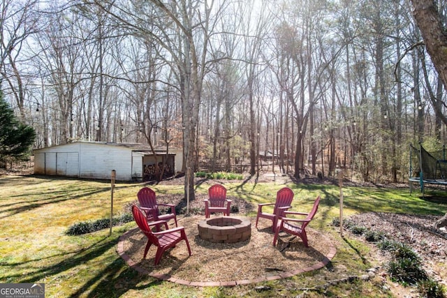 view of yard featuring an outdoor fire pit, a trampoline, and an outdoor structure