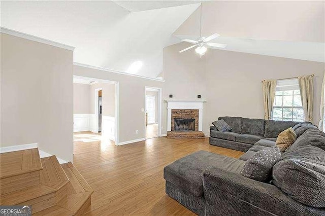 living room featuring a ceiling fan, wainscoting, a stone fireplace, wood finished floors, and high vaulted ceiling