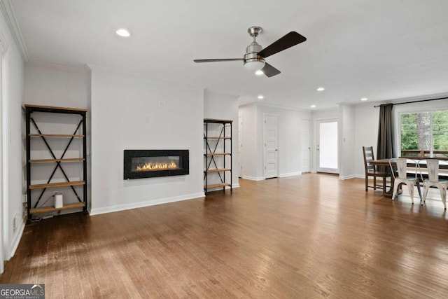 living area with recessed lighting, wood finished floors, baseboards, ornamental molding, and a glass covered fireplace