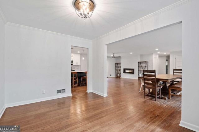 dining space with wood finished floors, visible vents, baseboards, ornamental molding, and a glass covered fireplace