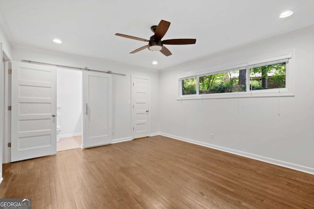 unfurnished bedroom with recessed lighting, a barn door, ornamental molding, wood finished floors, and baseboards