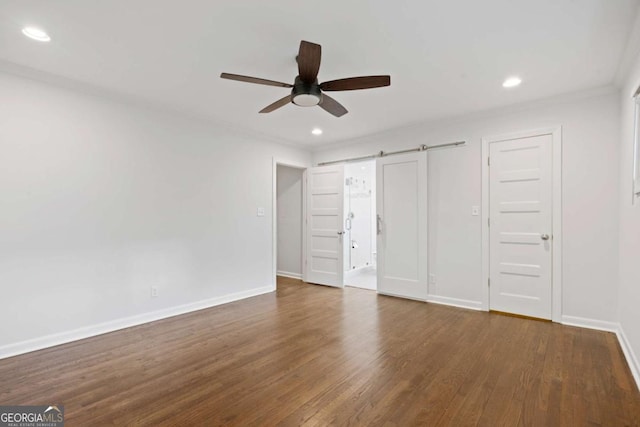 unfurnished bedroom featuring a barn door, baseboards, wood finished floors, and recessed lighting