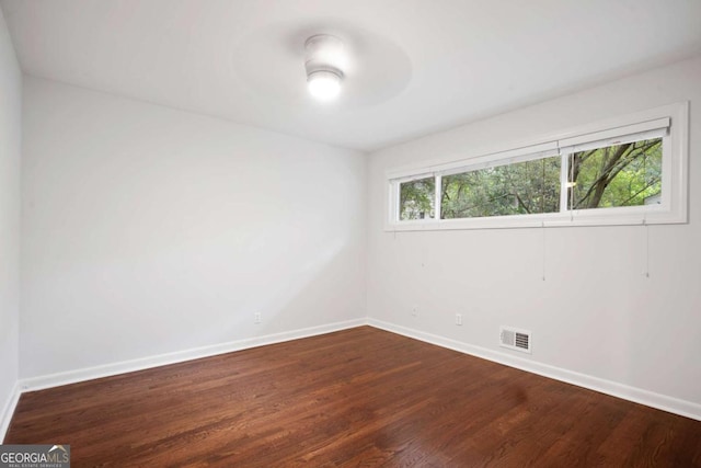 spare room featuring dark wood-style floors, a ceiling fan, visible vents, and baseboards