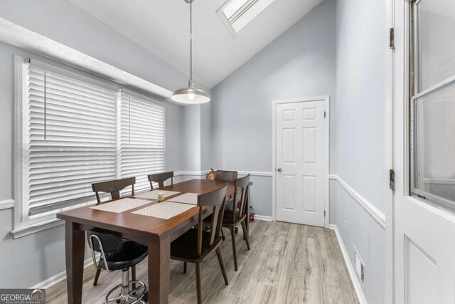 dining area with visible vents, vaulted ceiling with skylight, light wood-style flooring, and baseboards