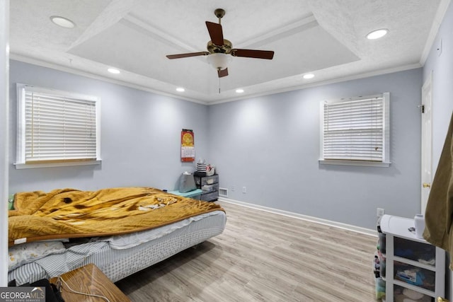 bedroom with a tray ceiling, recessed lighting, ornamental molding, wood finished floors, and baseboards