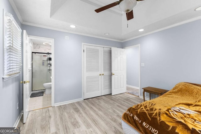 bedroom featuring wood finished floors, baseboards, a closet, a raised ceiling, and crown molding