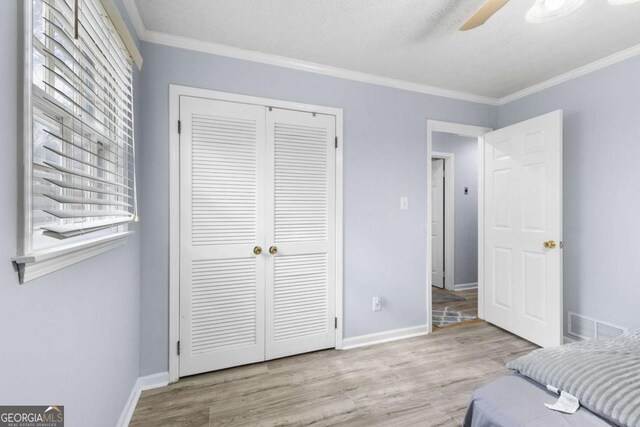 bedroom featuring a closet, visible vents, ornamental molding, wood finished floors, and baseboards