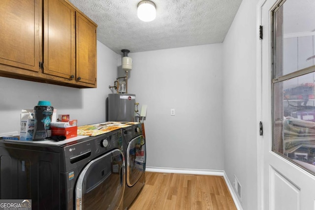 laundry room with a textured ceiling, light wood-style floors, water heater, cabinet space, and washer and clothes dryer