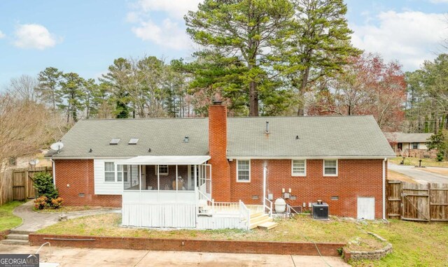 back of property featuring brick siding, a chimney, central air condition unit, a sunroom, and fence