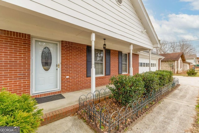 entrance to property featuring a garage, covered porch, and brick siding