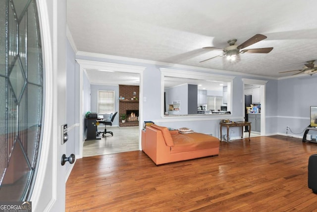 living room featuring a fireplace, wood finished floors, a ceiling fan, baseboards, and ornamental molding