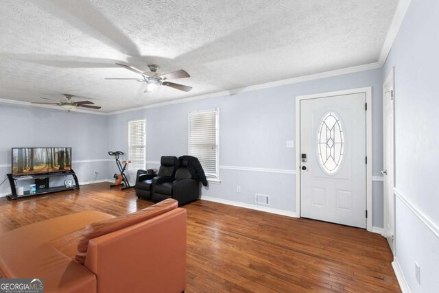 living area with a textured ceiling, hardwood / wood-style flooring, visible vents, baseboards, and ornamental molding