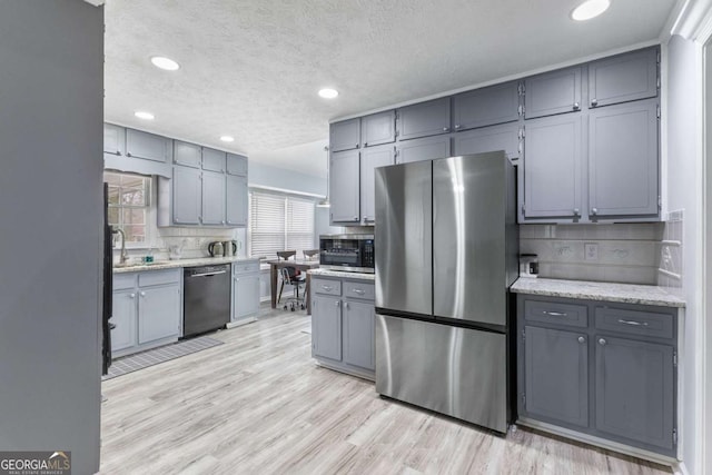 kitchen featuring stainless steel appliances, gray cabinets, light wood-style floors, and backsplash