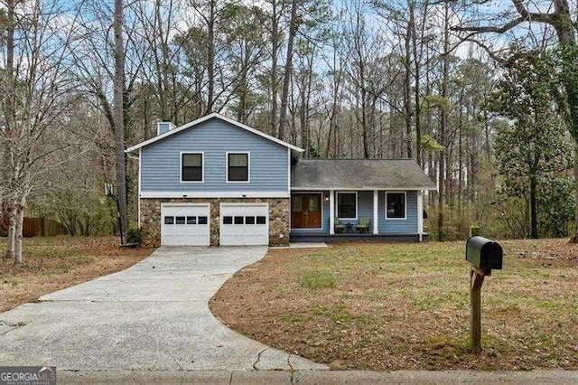 tri-level home featuring an attached garage, stone siding, a front yard, and driveway