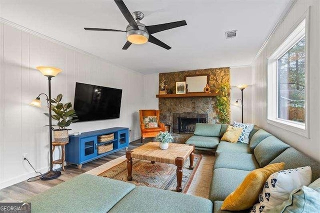 living area with a fireplace, wood finished floors, visible vents, a ceiling fan, and crown molding