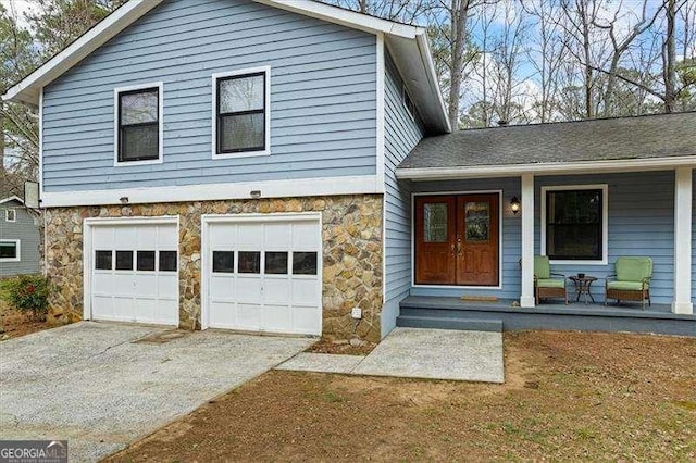 split level home with a garage, stone siding, driveway, and a porch