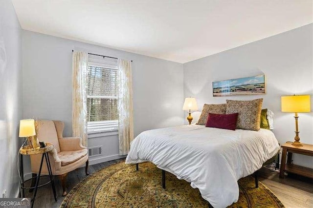 bedroom with baseboards, visible vents, and wood finished floors